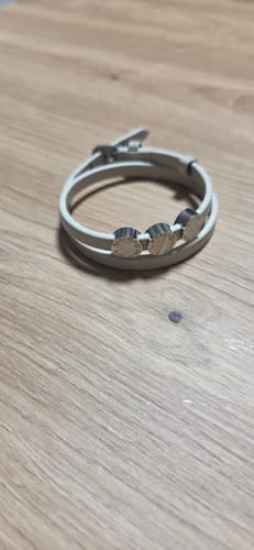 Customer's Liora bracelet with a light-colored band and three engraved charms on a wooden surface.