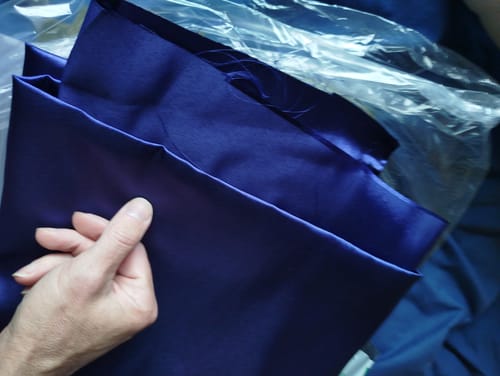 Reviewer's hand holding the shiny, navy satin fabric to display its deep color and texture.