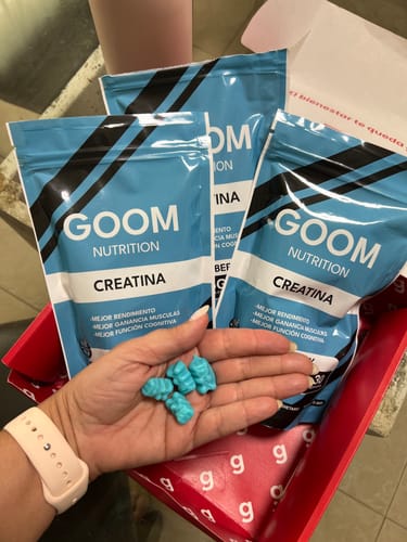 Cliente sosteniendo varias gomitas de creatina azules en forma de oso en su mano, con el empaque del producto de fondo.