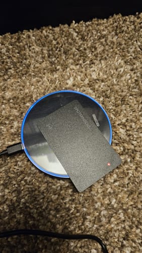 Customer's SPOTMINDERS. Tracking Card with a red light on a round wireless charging pad.