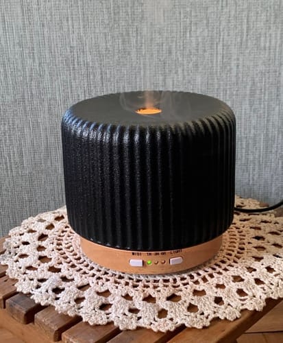 Ein Kunde zeigt den schwarzen Live Slow Aroma Diffuser in Betrieb auf einem Holztisch.