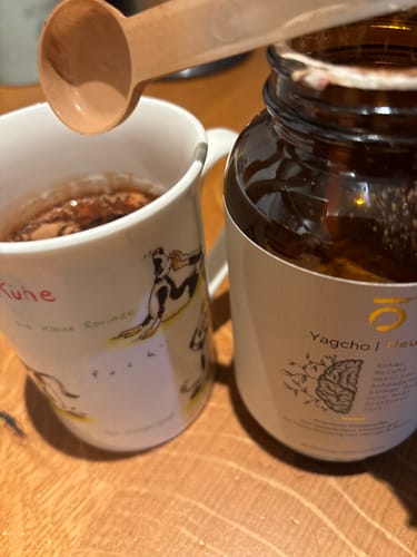 Rezensent gibt einen Löffel Pulver aus einem Glasgefäß in eine Tasse.