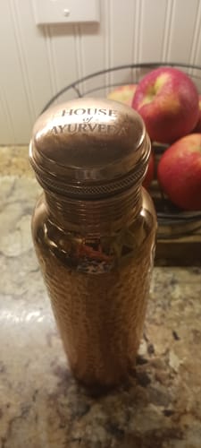 Close-up of a customer's hand-hammered Pure Copper Water Bottle on a kitchen counter.