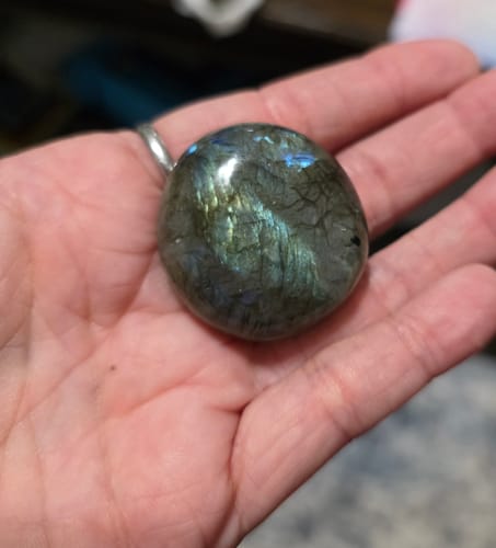 Customer's hand holding a polished labradorite crystal with blue iridescence.