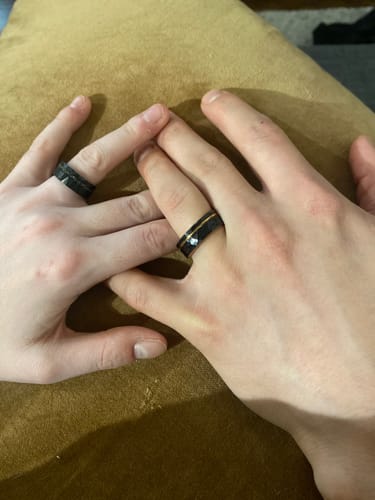 A customer's hand wearing the hammered black Apollo ring next to their fiancé's hand, which also wears a ring.