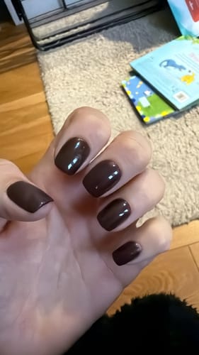 Customer's hand showing short, square Cherry Cola press-on nails with a glossy dark finish.