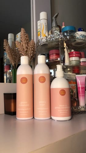 Reviewer's three Glossy Basics products, including a shampoo and conditioner, on a vanity.