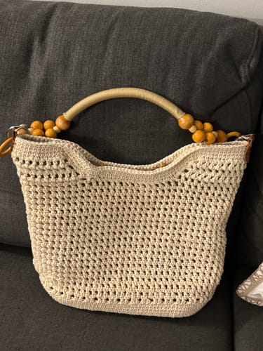 Customer's completed Sunny Beach Tote, an off-white crochet bag with a beaded handle, resting on a dark couch.