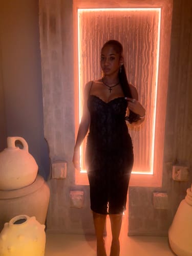 Reviewer standing in the black Stretch Lace Midi Dress in front of a glowing rectangular light.