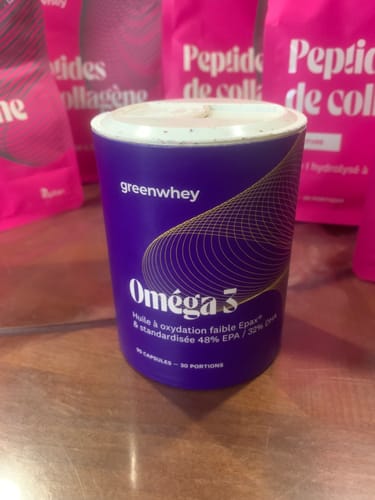 Photo d'un client montrant le pot violet d'Oméga 3 EPAX® sur une table en bois.