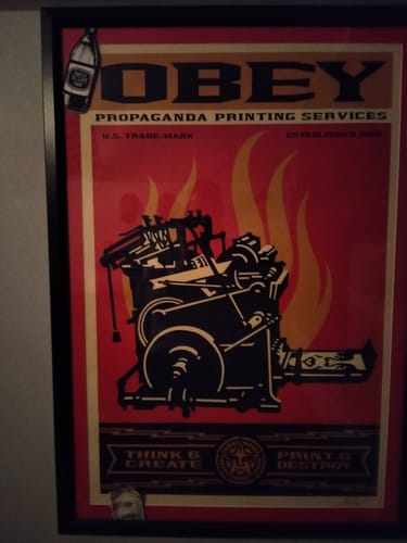 Reviewer's SCREW UP STICKER, shaped like an Old English bottle, on a framed poster.