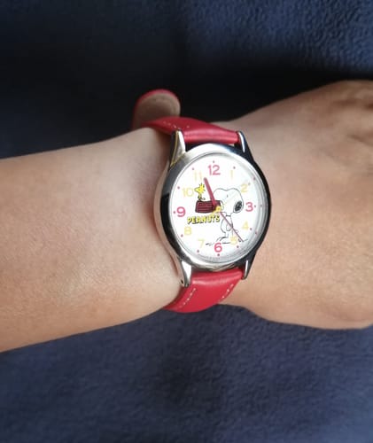 Cliente mostrando el reloj Q&Q de Snoopy con correa roja en su muñeca.
