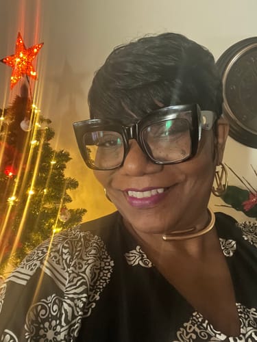 Customer smiling while wearing a short, black pixie-cut wig and large glasses in front of a Christmas tree.