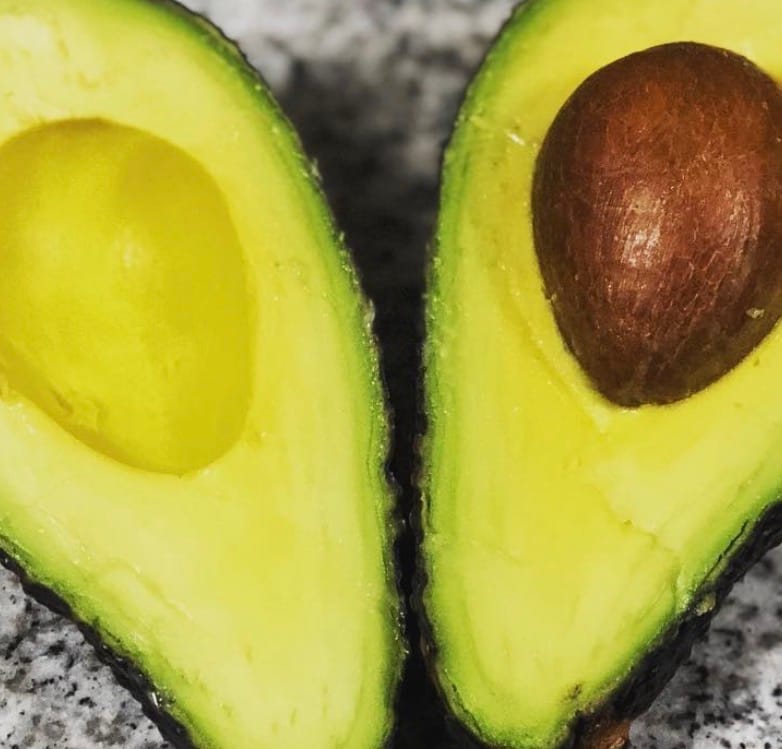Cliente muestra una palta Hass cortada por la mitad, revelando su pulpa cremosa y de color verde claro.