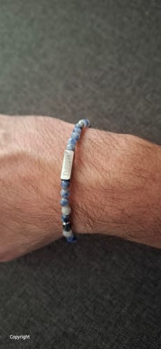 A close-up of a customer wearing the Tribute Blue Sodalite bracelet on their wrist, showing the blue beads and silver pendant.