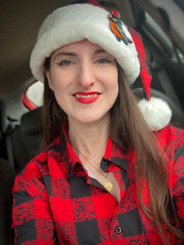 Customer smiling while wearing the plaid 'Lumberjack' Santa Hat with a plush white brim and matching shirt.