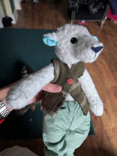 Customer holds a handmade white toy bear made with the wool blend remnants, wearing a small plaid waistcoat.
