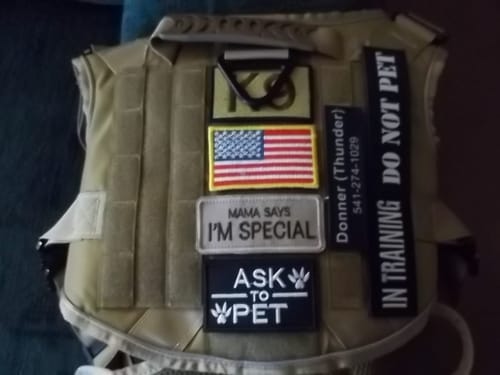 A customer's tan Tactical K9 Dog Harness laid flat, customized with multiple hook-and-loop patches.