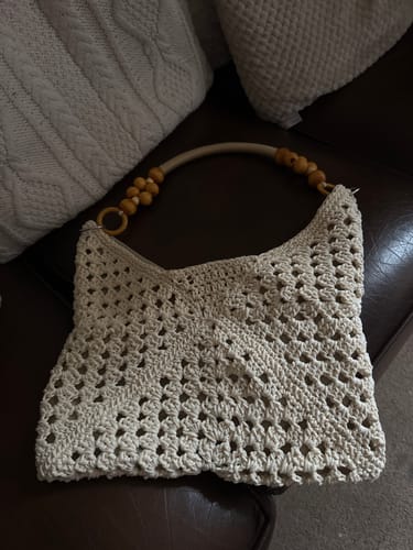Customer's completed Sunny Holiday shoulder bag, shown in cream with its wood handle on a sofa.