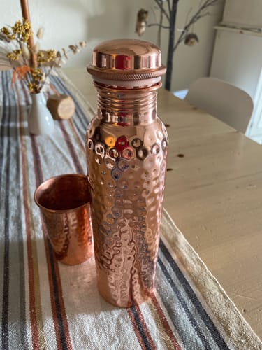 Customer's hand-hammered Pure Copper Water Bottle and matching tumbler displayed on a striped table runner.