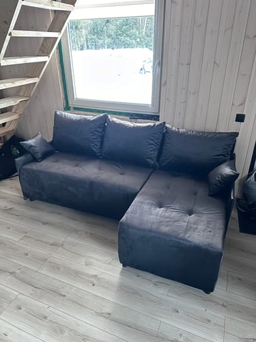 Kliento tamsiai pilkas minkštas kampas „Monak“ kambaryje su šviesiomis medinėmis grindimis.