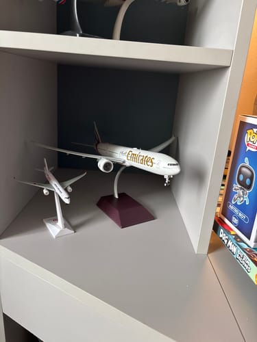Reviewer's Emirates 777-300ER model airplane displayed on its stand on a shelf.