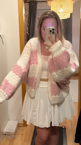 Kundin trägt den weichen Bold Stripes Oversized Cardigan in Rosa und Weiß zu einem Rock.