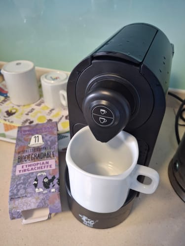 Reviewer's box of Cowpresso Ethiopian Yirgacheffe capsules sits next to a black Nespresso machine with a white mug.