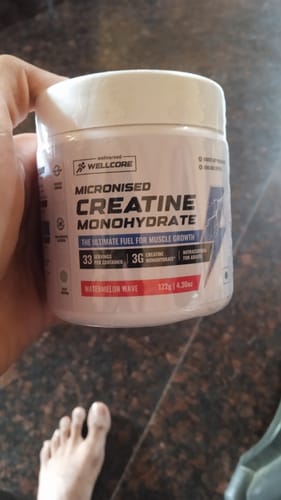 Reviewer holding a white tub of Wellcore Micronised Creatine Monohydrate in the Watermelon Wave flavor.