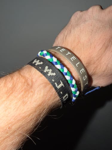 Customer wearing the woven DAVID Bracelet in blue, green, and white on their wrist with two other bracelets.