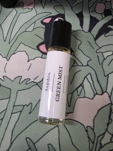 Customer's Green Mist Perfume Oil rollerball bottle resting on a green and white floral patterned surface.