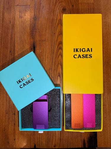 Reviewer's 2-Pack Bundle of metal pill cases. The purple, orange, and pink cases are shown inside their colorful open boxes.