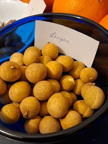 Rezensent zeigt die runden Longan-Früchte in einer blauen Schüssel.