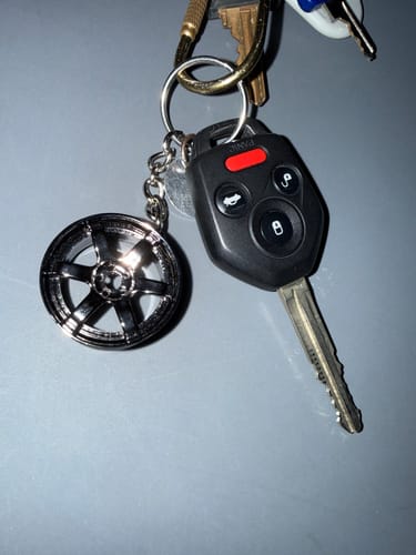 Customer's TE Wheel Keychain attached to a car key fob on a keyring against a grey surface.