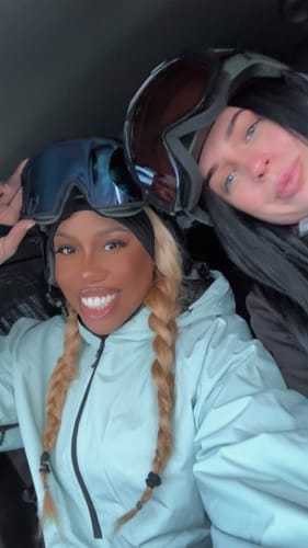 Reviewer smiling in their ice blue half-zip snow anorak while wearing snow goggles with a friend.