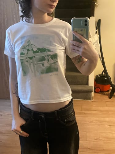 Reviewer taking a mirror selfie in the 'a dip in the pool' baby tee to show its cropped fit.