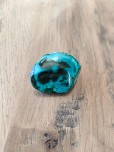 Pierre Chrysocolle-Malachite polie d'un client, aux couleurs bleues et vertes vives, posée sur une surface en bois.