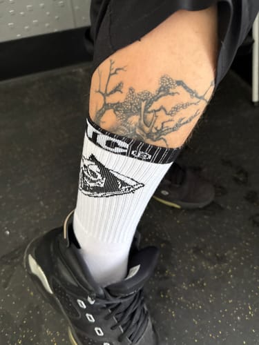 Close-up of a customer wearing the white Reaper Crew Socks with a black graphic and black sneakers.