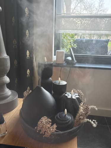 Recensent toont een zwarte Geurwolkje diffuser die een wolkje nevel verspreidt in een huiselijke setting.