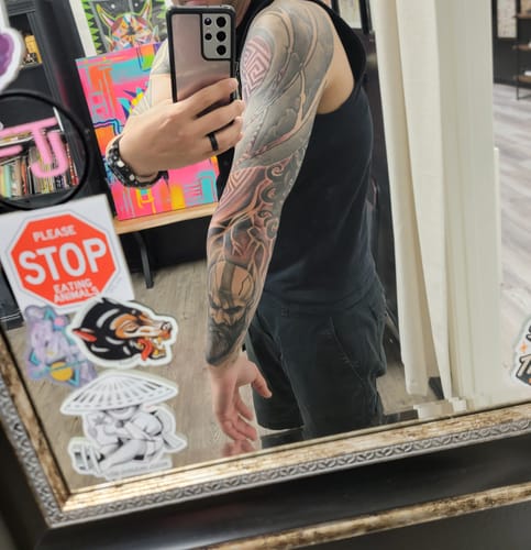 Reviewer's mirror selfie showing a full, detailed sleeve tattoo on their left arm, a result of using the numbing cream.