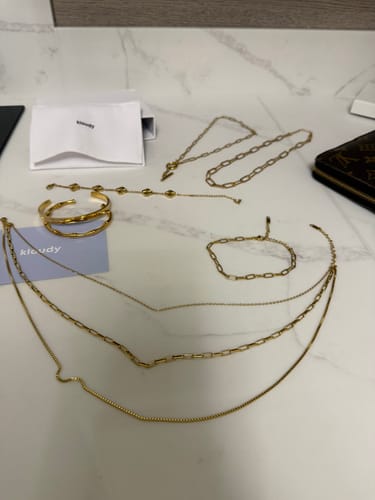Customer's collection of gold-colored jewelry, including necklaces and bracelets, laid out on a marble surface.