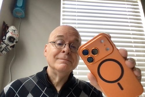 Reviewer holding up the orange MagCase Metal phone case, showing the back with the MagSafe ring.