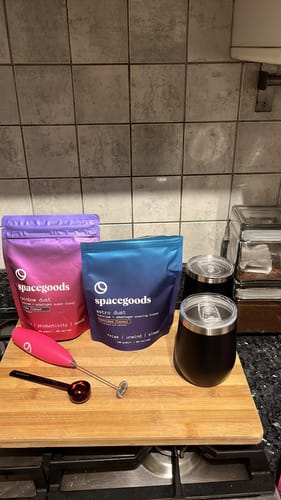 Customer's Day + Night Comboproduct pouches, Rainbow Dust and Astro Dust, on a wooden board with a frother and travel mug.