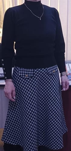 Recenzent purtând setul Faustina, compus dintr-o bluză neagră cu guler înalt și o fustă în carouri.