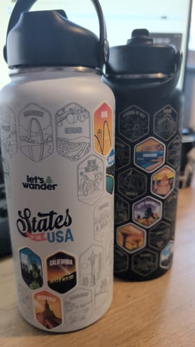 Reviewer's white 50 States Bottle with several colorful stickers applied, standing next to another black bottle.