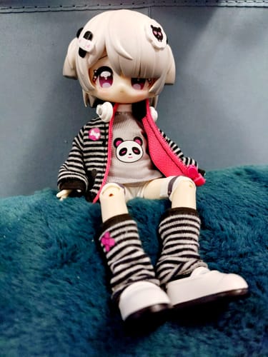 Customer's Breaktime Sprint BJD figure sits on a blue cushion, wearing a panda shirt and an unzipped striped hoodie.
