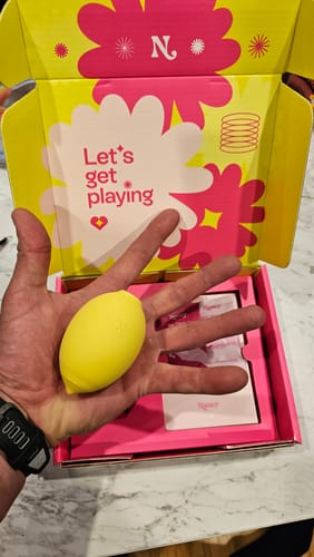 Reviewer holding the yellow, lemon-shaped Lem Clitoral Massager in their hand above its open box.