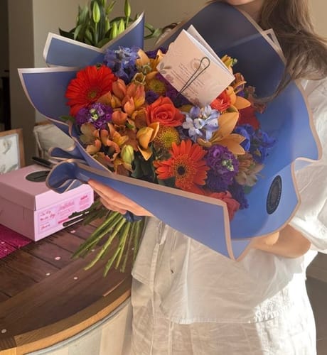 A reviewer holding their large, colorful Mood Booster bouquet wrapped in blue paper.