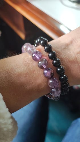 Client portant son bracelet Auralite 23 aux perles violettes à côté d'un bracelet noir.