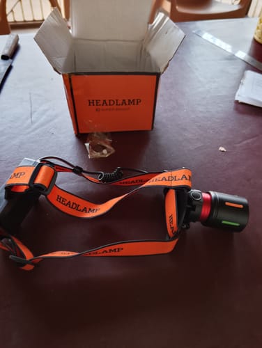Customer's rechargeable headlight with orange straps displayed on a table next to its open box.